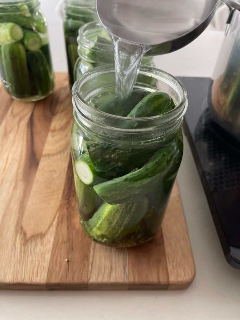 brine getting poured over cucumbers packed into a Mason jar