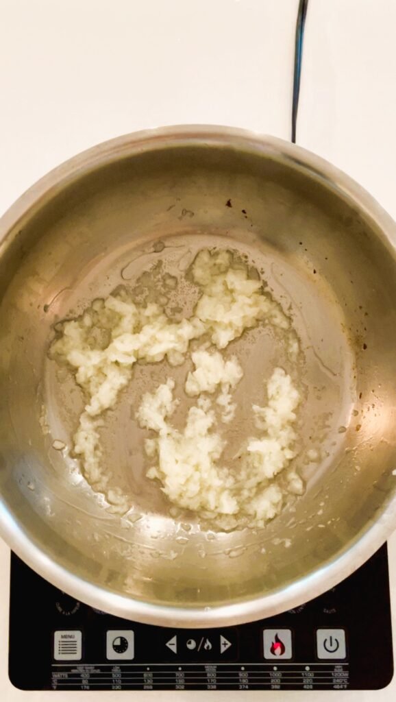 minced onion is getting fried in oil on a stove in a heavy bottomed wide pot