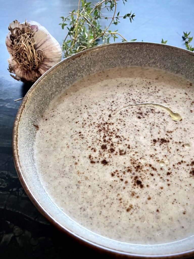 creamy sunchoke soup served in a bowl with a drizzle of oil and truffle powder dust on top