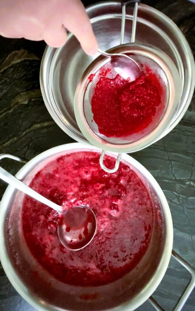 pushing raspberry mixture through a fine mesh strainer to remove the seeds