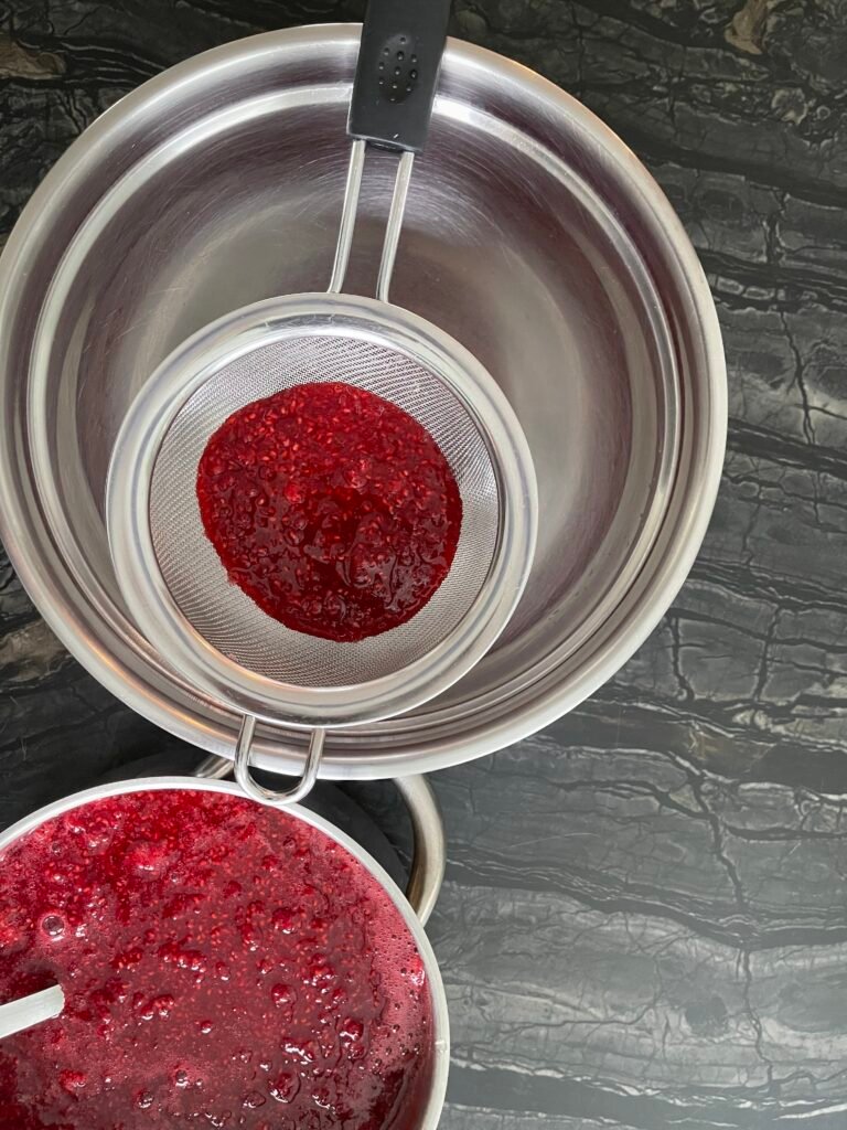 straining raspberry seeds using a fine metal mash strainer