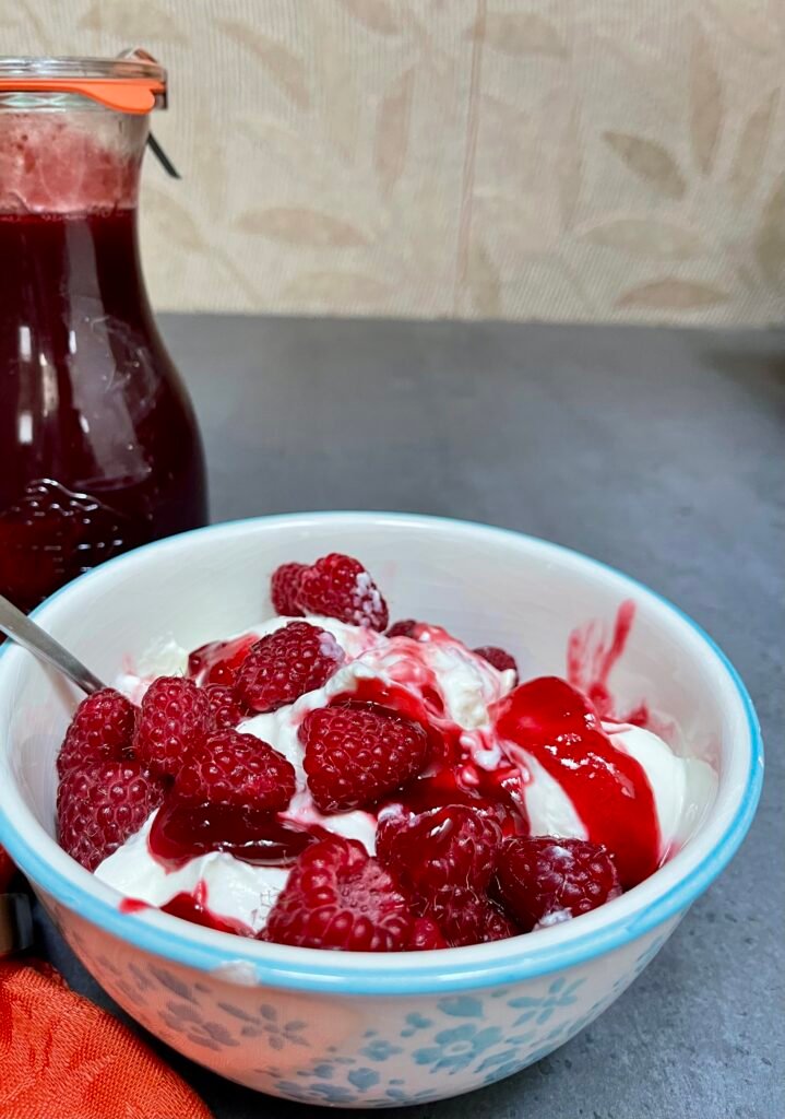 Raspberry syrup serving suggestion. A bowl of yoghurt with raspberry drizzled with raspberry syrup