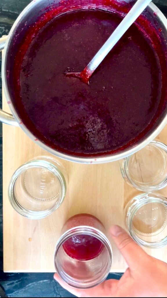 ladle cooked huckleberry jam into canning jars