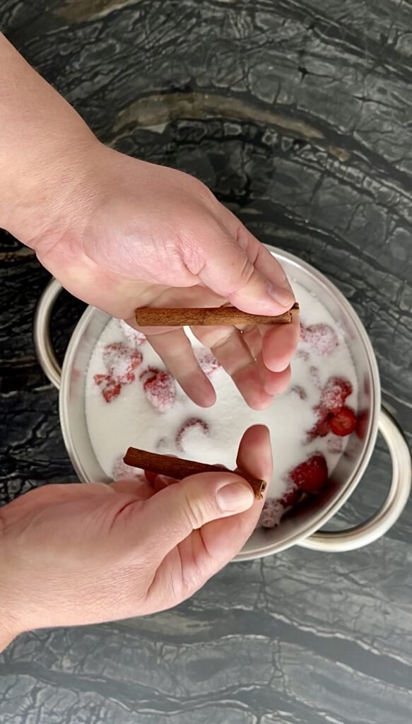 sugar and cinnamon stick get added to the hulled strawberries in a pot