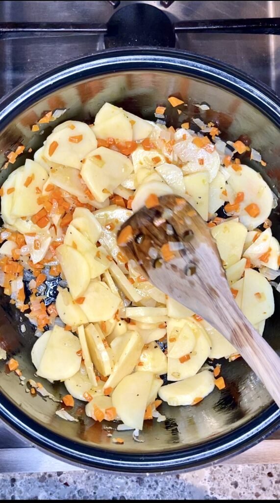 sliced potatoes are added to the pot with partially cooked carrots and onions