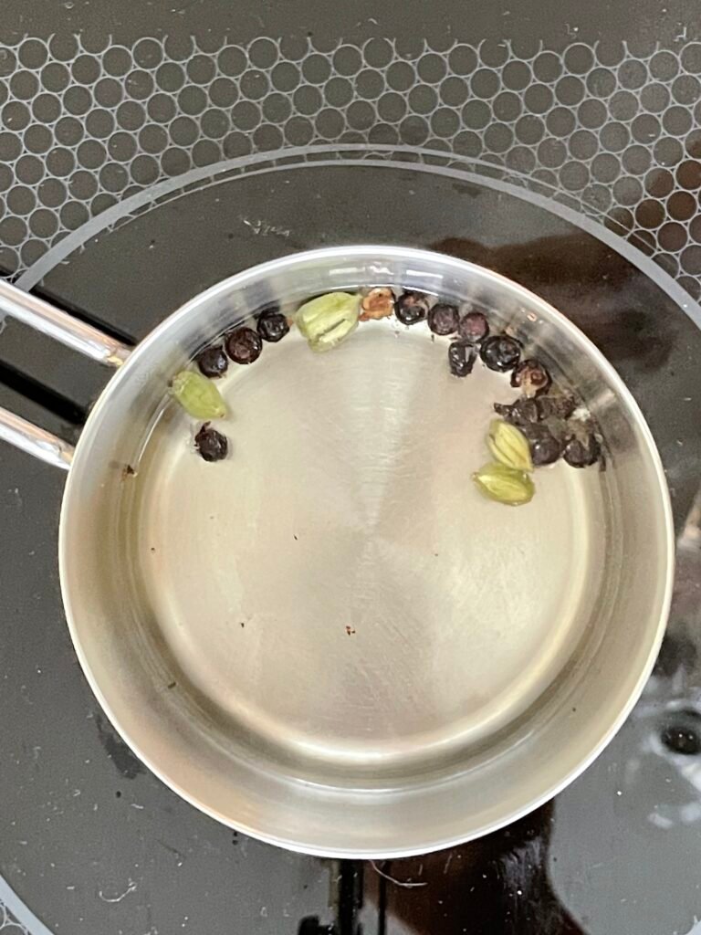 cardamom pods and crushed juniper berries infusion is being prepared in a small sauce pan