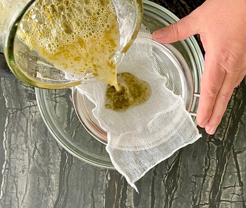 Apple lemon balm jelly pouring blended mixture through cheesecloth strainer