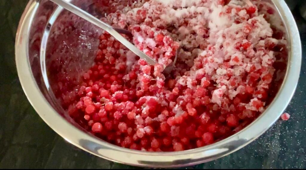 Mashing huckleberries with sugar using potato masher