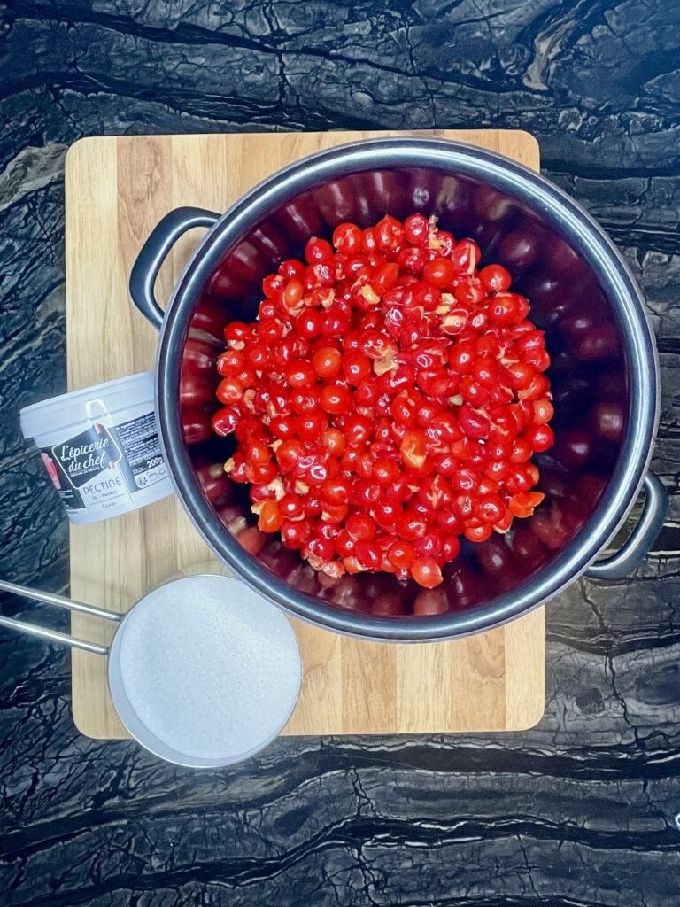 pitted  sour cherries in the pot, bucket of pectin and a bowl of sugar - ingredients of this recipe on the table