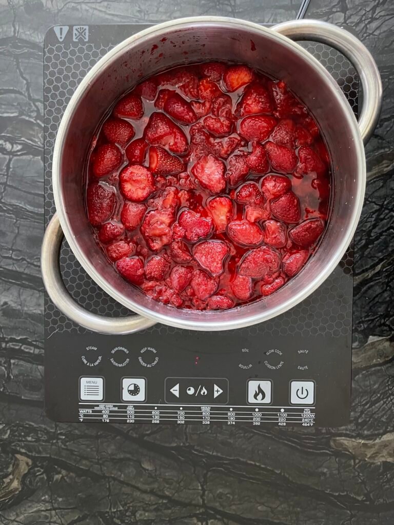 Pot of strawberries mixed with sugar and lime zest sitting on an induction cooktop before cooking