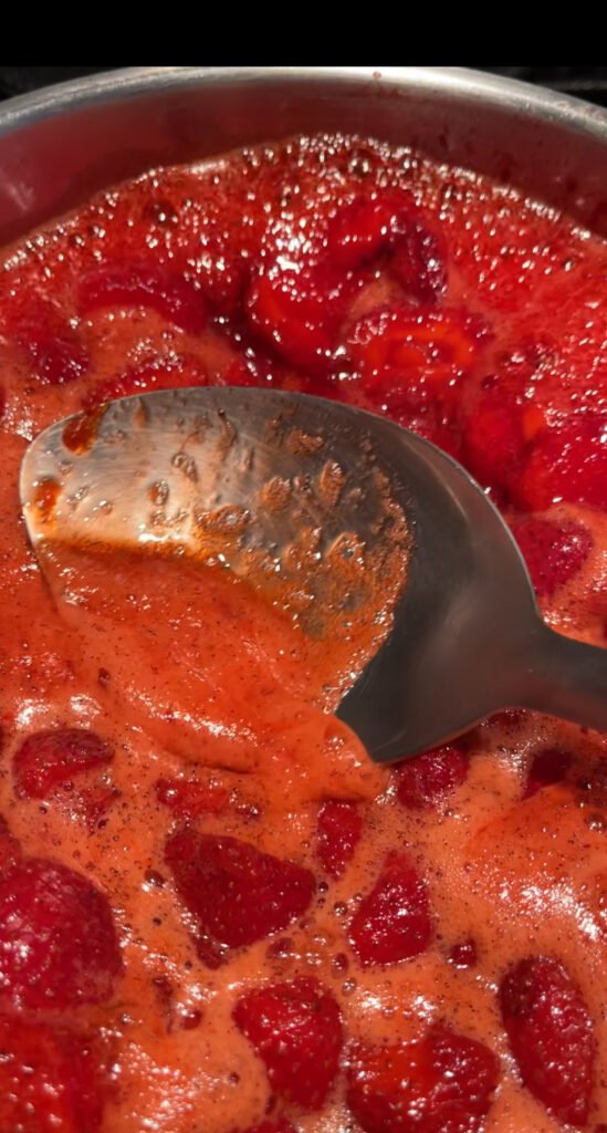 spoon skimming foam from the surface of cooking strawberry lime jam.