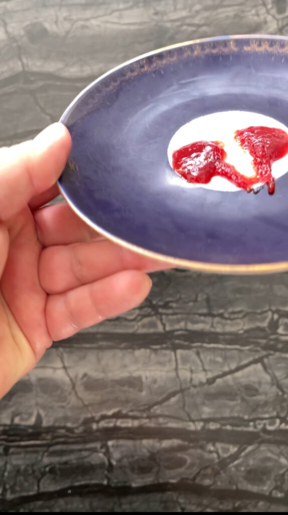 Hand holding a chilled plate with a dollop of strawberry lime jam, testing for a wrinkled se