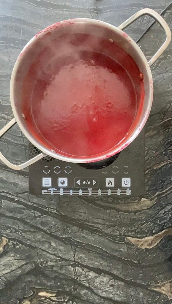 Overhead shot of a pot of red ketchup base simmering on an induction cooktop.