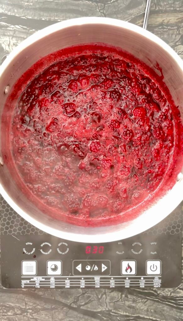 Macerated raspberry mixture simmering in a pot before straining