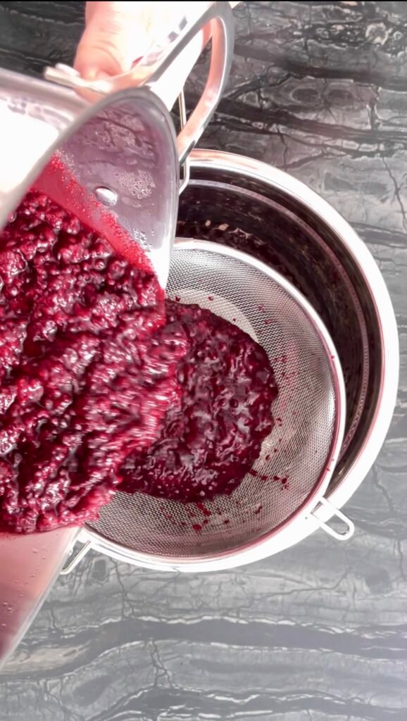 Pouring cooked blackberry mixture through a mesh strainer into a bowl