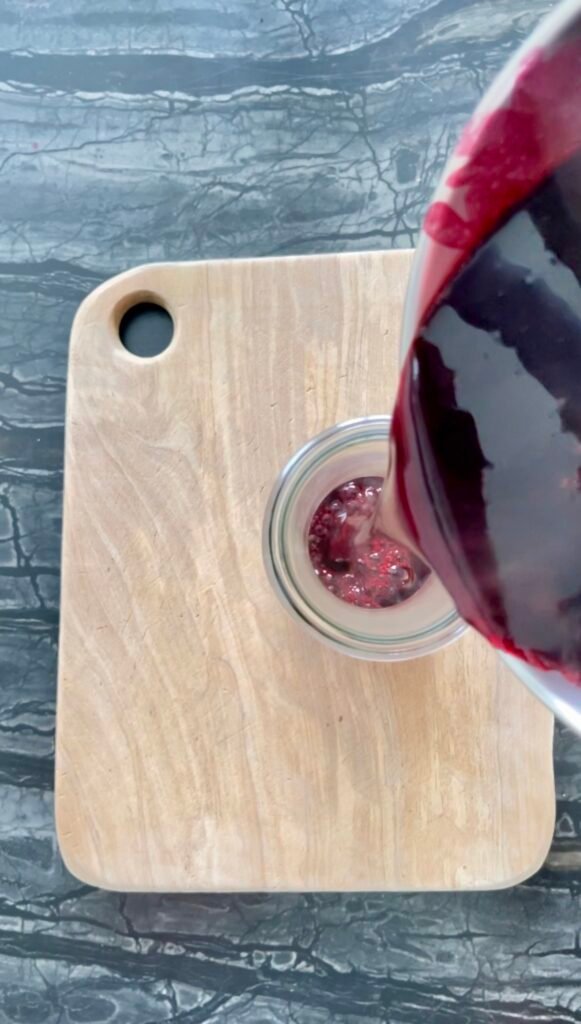 Pouring finished blackberry juice into a small glass jar