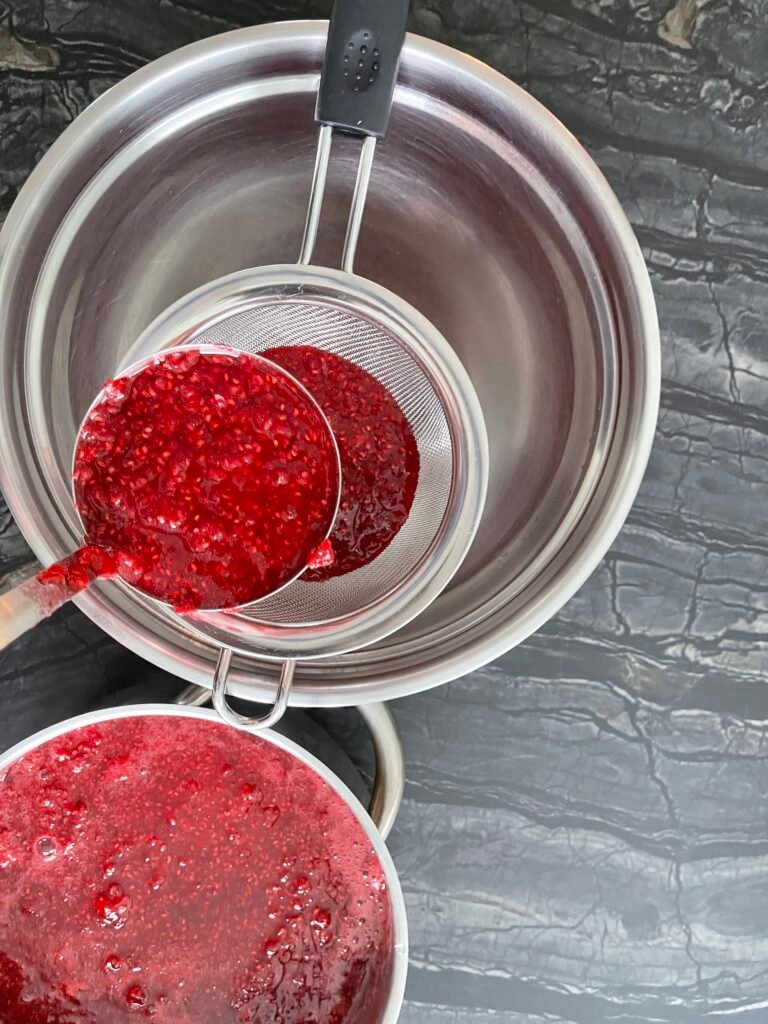 Raspberry mixture being strained through a fine mesh strainer into a bowl