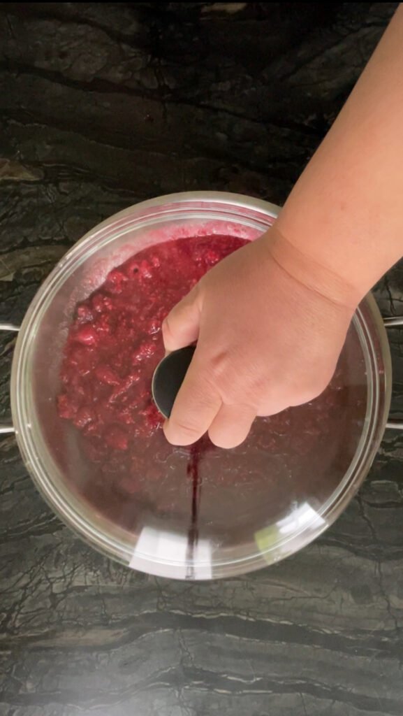 Hand pressing a lid onto a bowl of mashed raspberries before overnight maceration