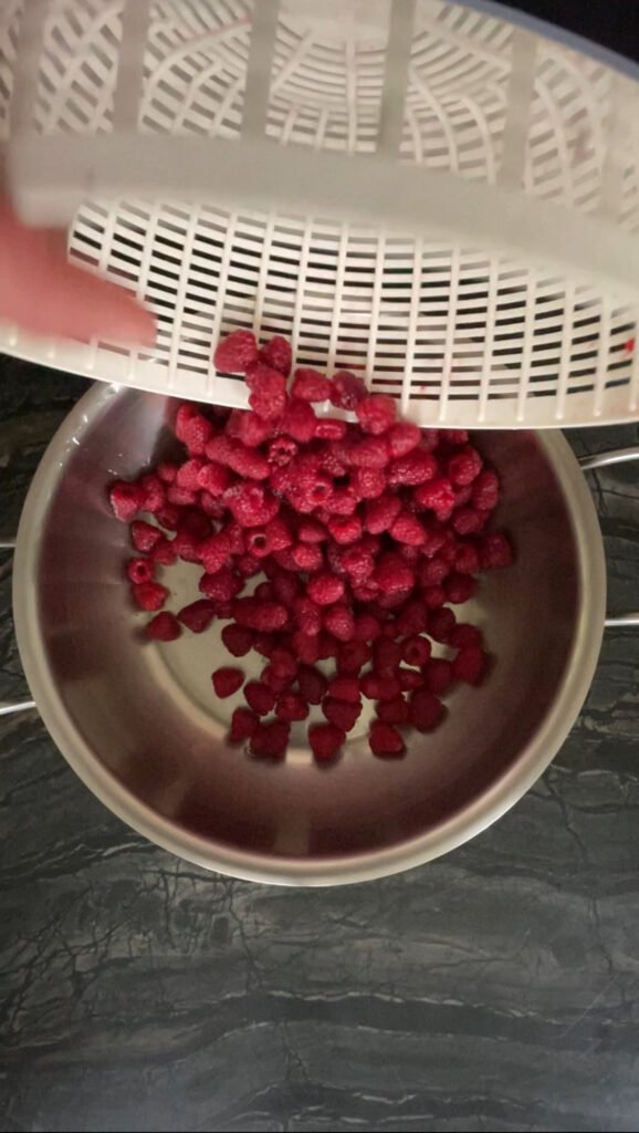 fresh raspberries being poured into a metal pot for berry juice