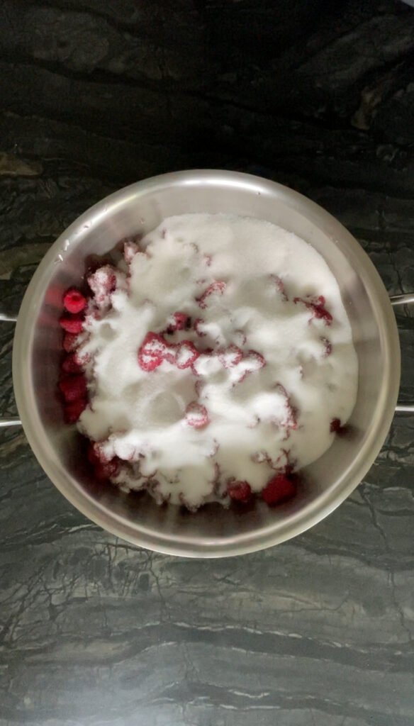 granulated sugar sprinkled over raspberries in a pot before maceration
