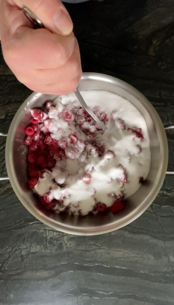 Hand mashing sugared raspberries to release juice for canning