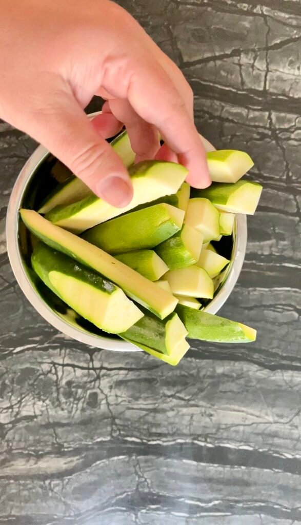Hand placing cut zucchini spears into a bowl for zucchini pickles