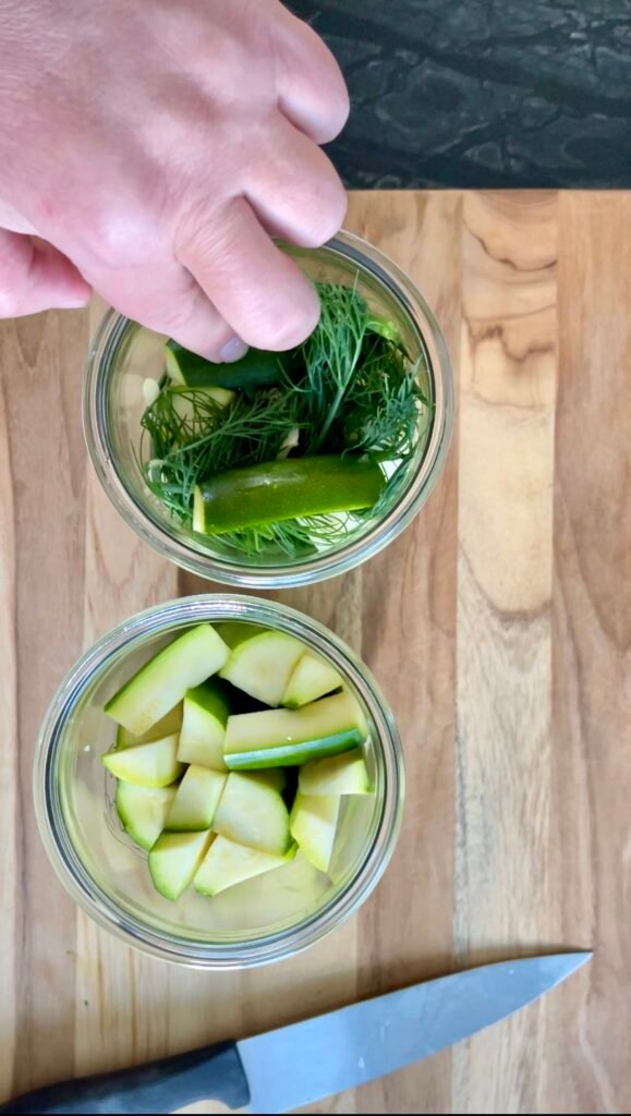 Packing fresh dill and zucchini spears into a jar with a paring knife nearby