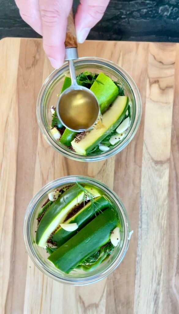 Adding apple cider vinegar spoon by spoon to jars of zucchini spears