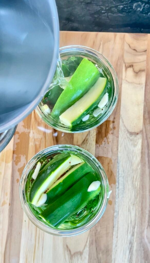 Pouring hot pickling brine from a pot into jars of zucchini spears