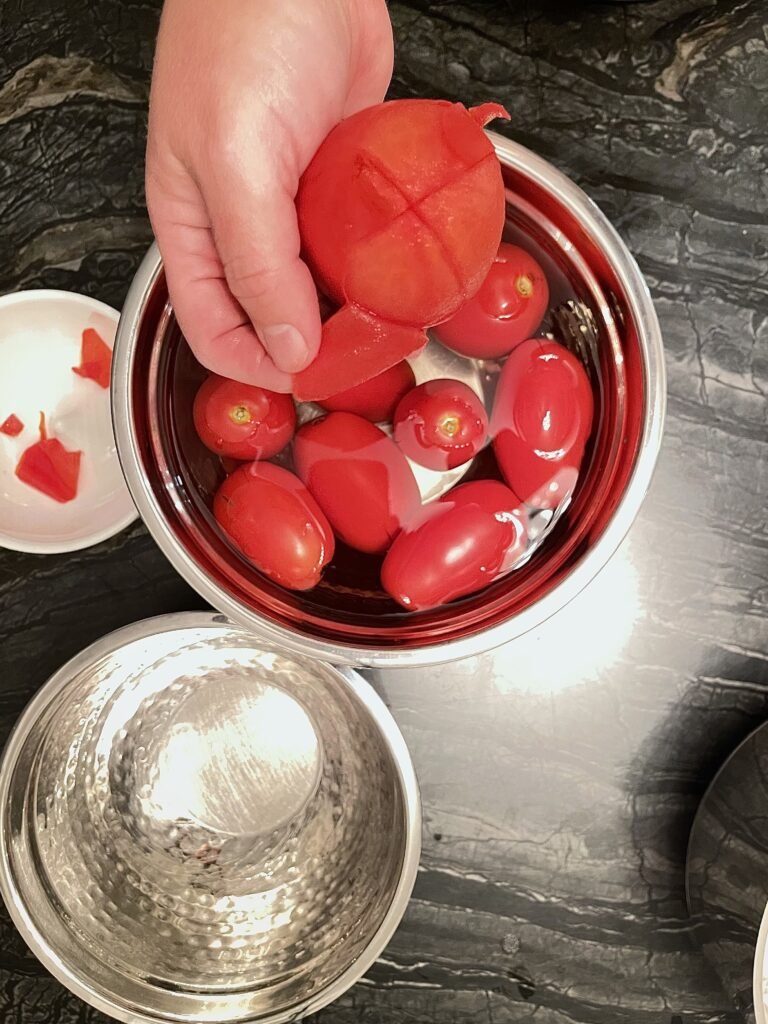 Tomato jam hand peeling skin from a blanched tomato