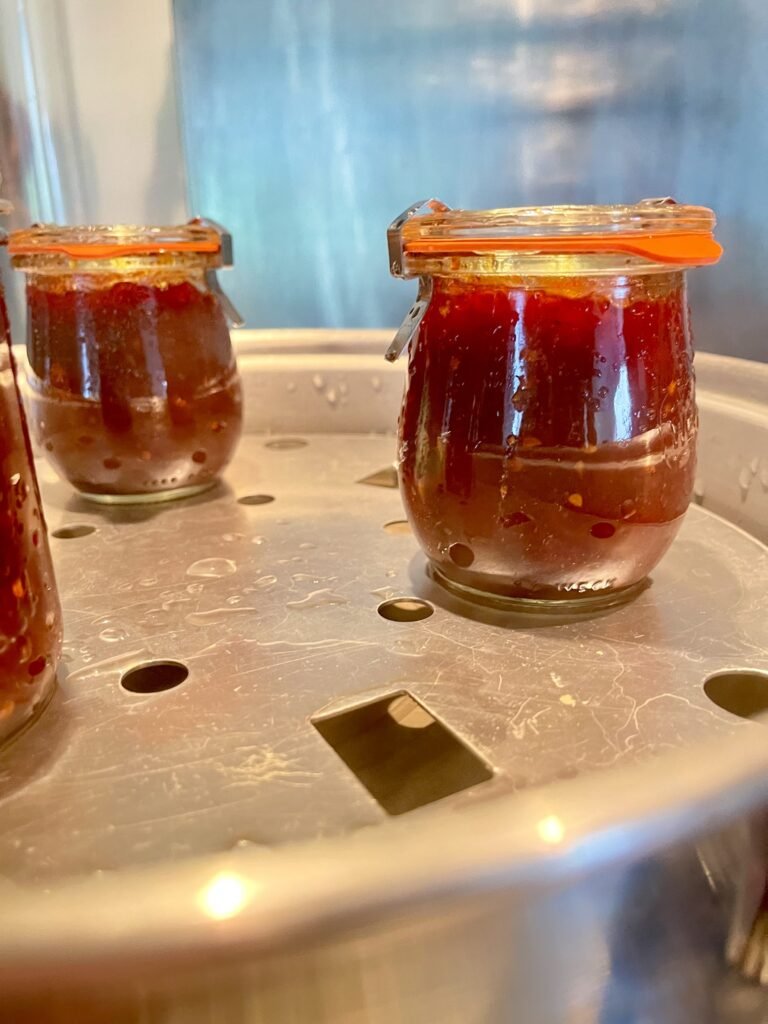 Tomato jam filled jars sitting on a rack in a steam canner