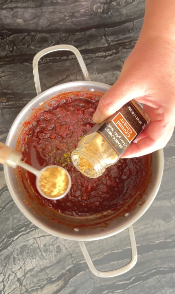 Tomato jam adding a spoonful of ground ginger