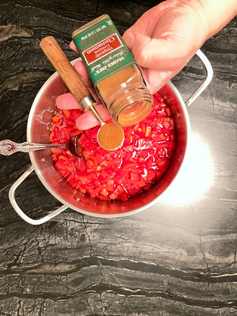 Tomato jam measuring ground cinnamon into a spoon