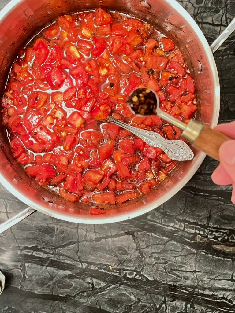 Tomato jam adding a spoonful of red pepper flakes to the tomatoes