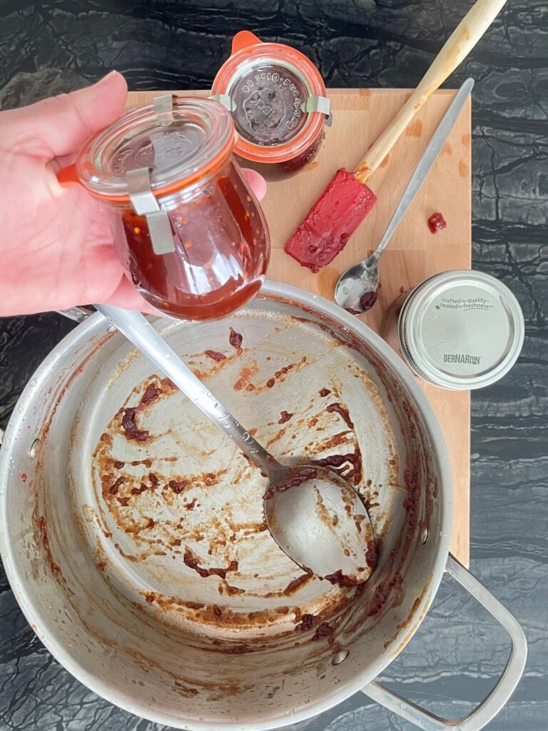 Tomato jam empty pot next to jars filled with finished jam