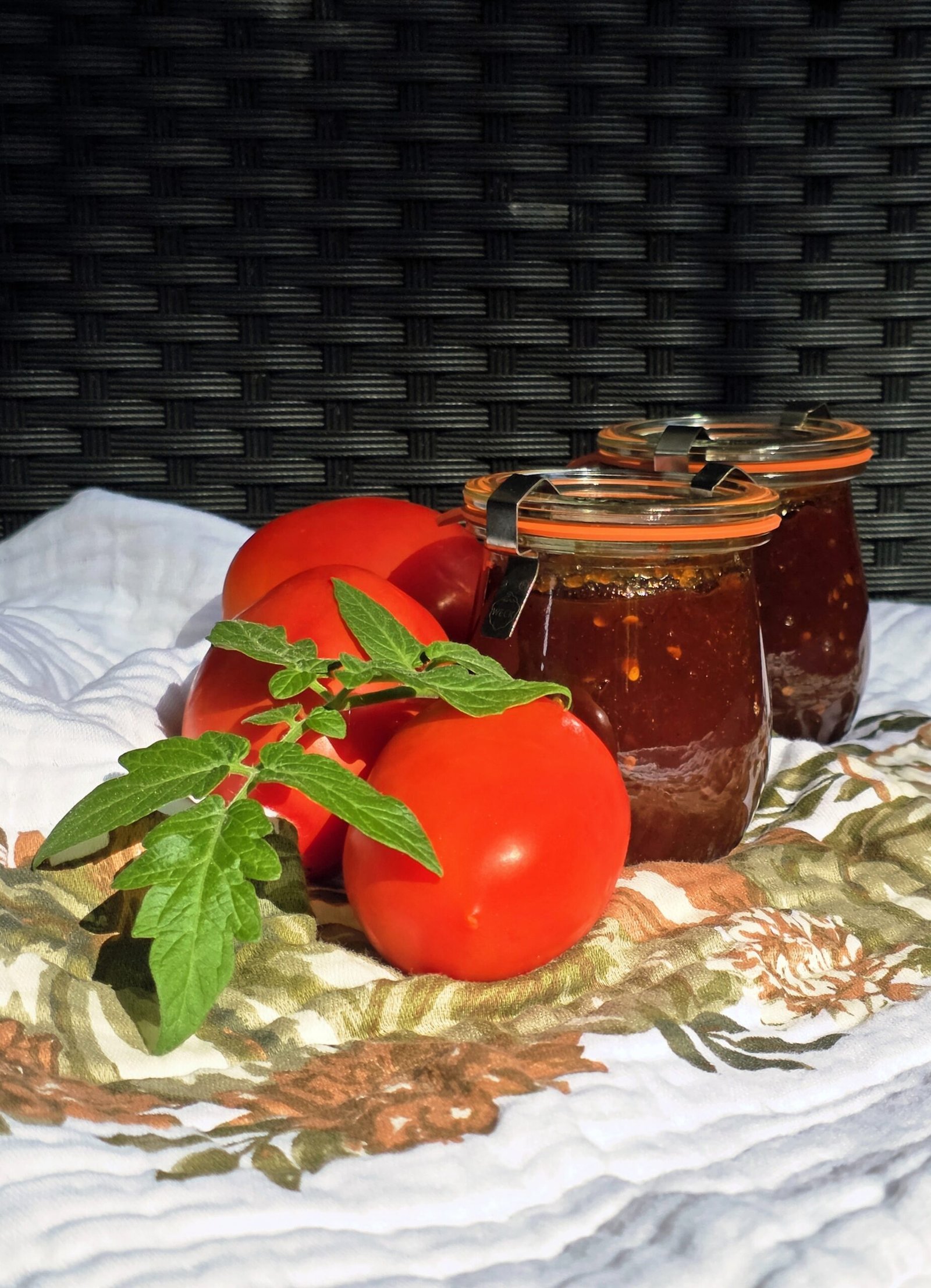 Tomato jam finished jars beside fresh whole tomatoes
