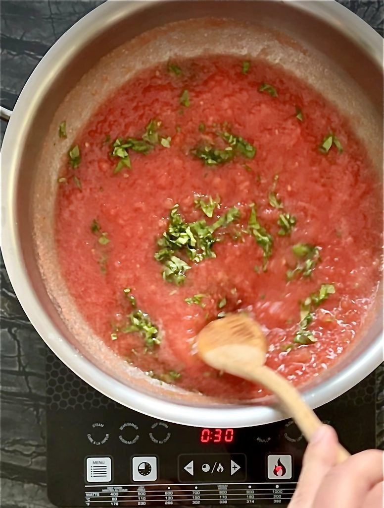 Crushed tomato sauce with chopped basil in a steel pot on an induction cooktop
