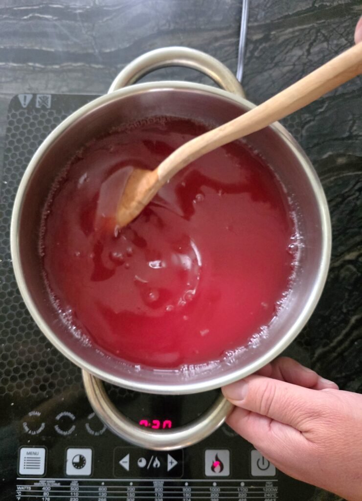 Wooden spoon stirring red crab apple juice in a pot on a cooktop