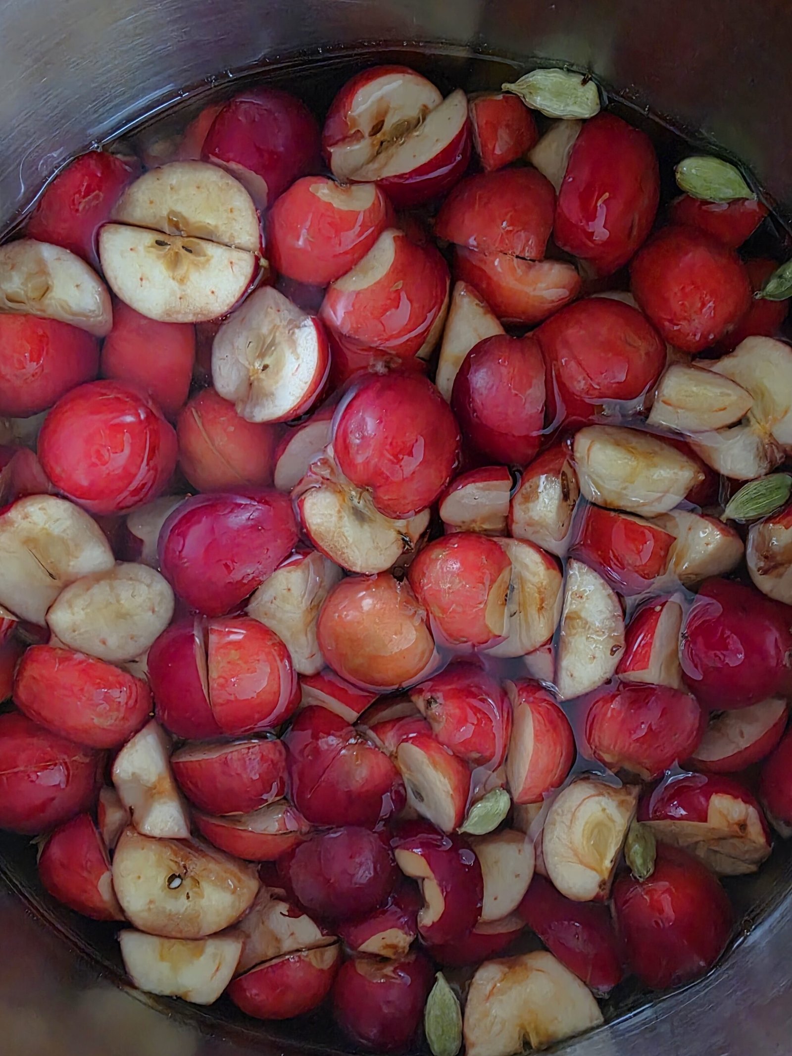 Pot of quartered red crab apples and green cardamom pods covered with water for crab apple jelly