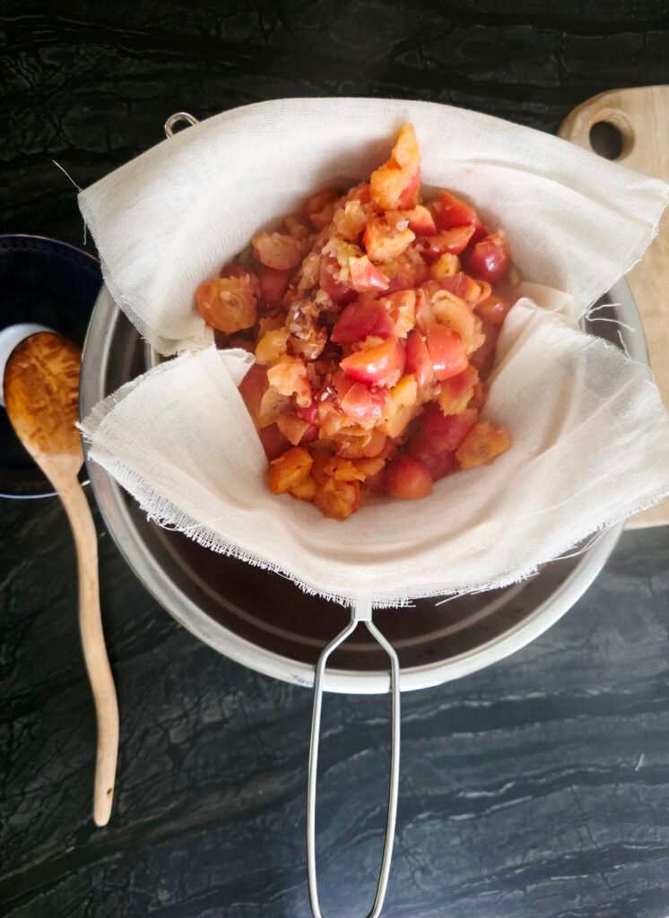 Cooked crab apples in a cheesecloth-lined strainer set over a bowl, with a wooden spoon beside it