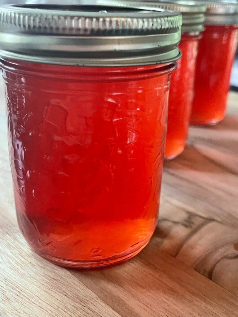 Jars of red crab apple jelly with metal lids lined up on a wooden counter