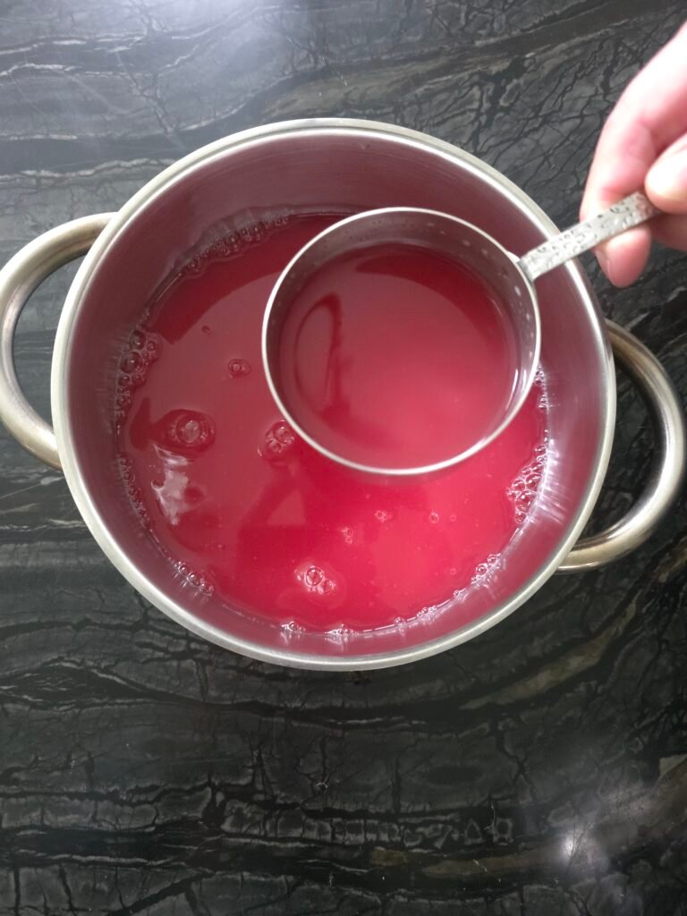 Measuring cup held over a pot of red crab apple juice