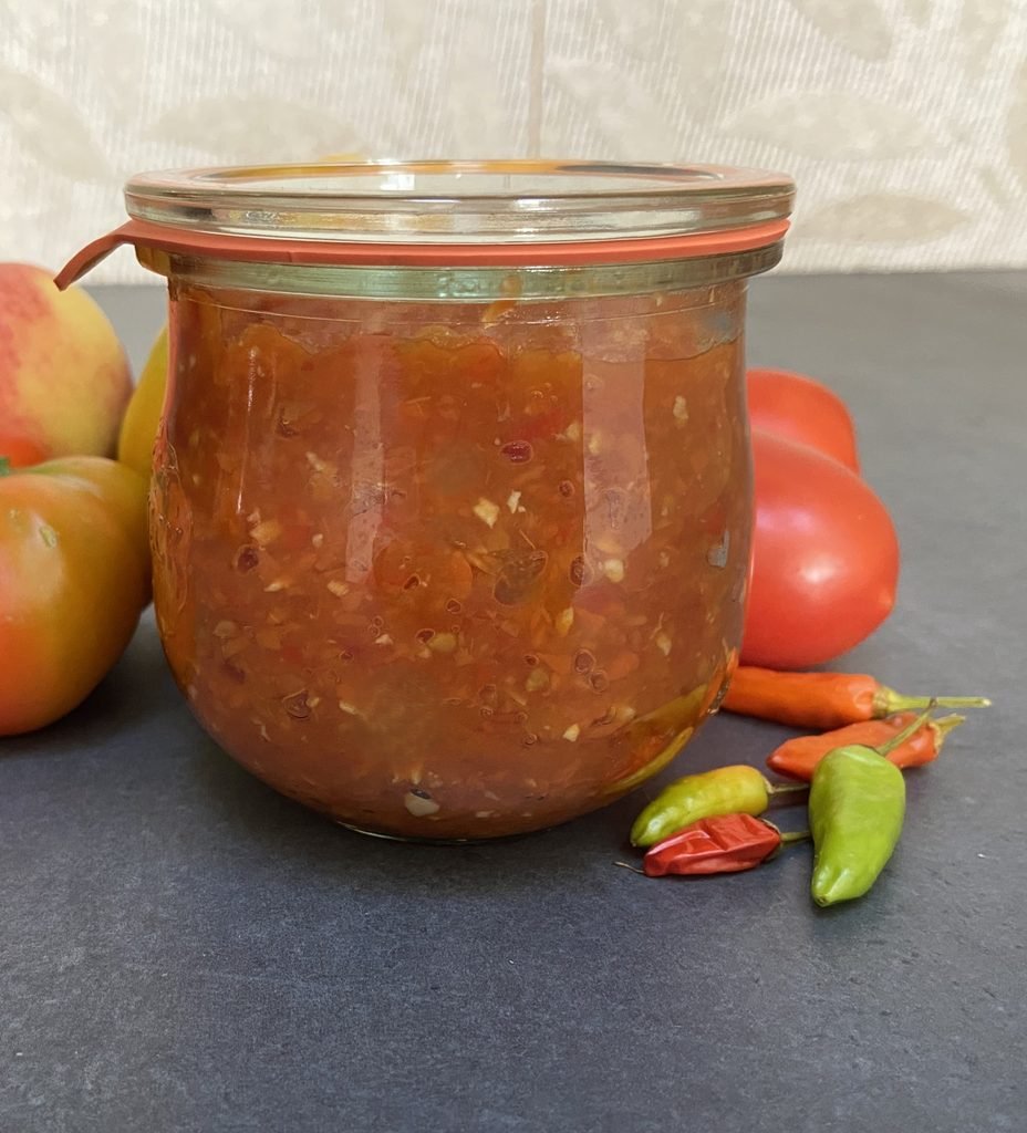 Weck jar of chunky tomato paste salsa with fresh tomatoes and hot peppers beside it