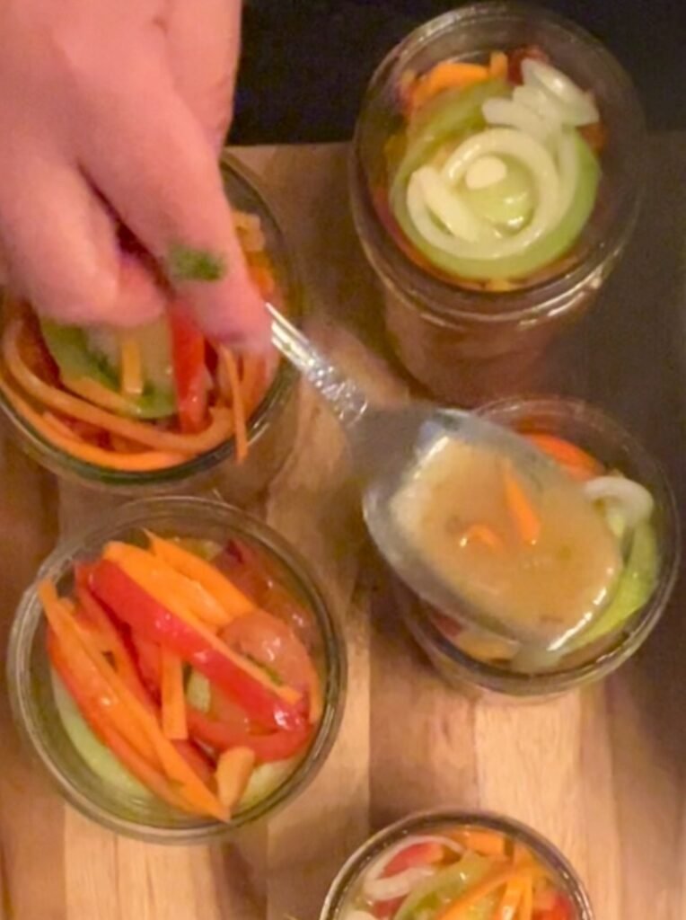 A ladle pouring golden liquid over vegetables in a jar.