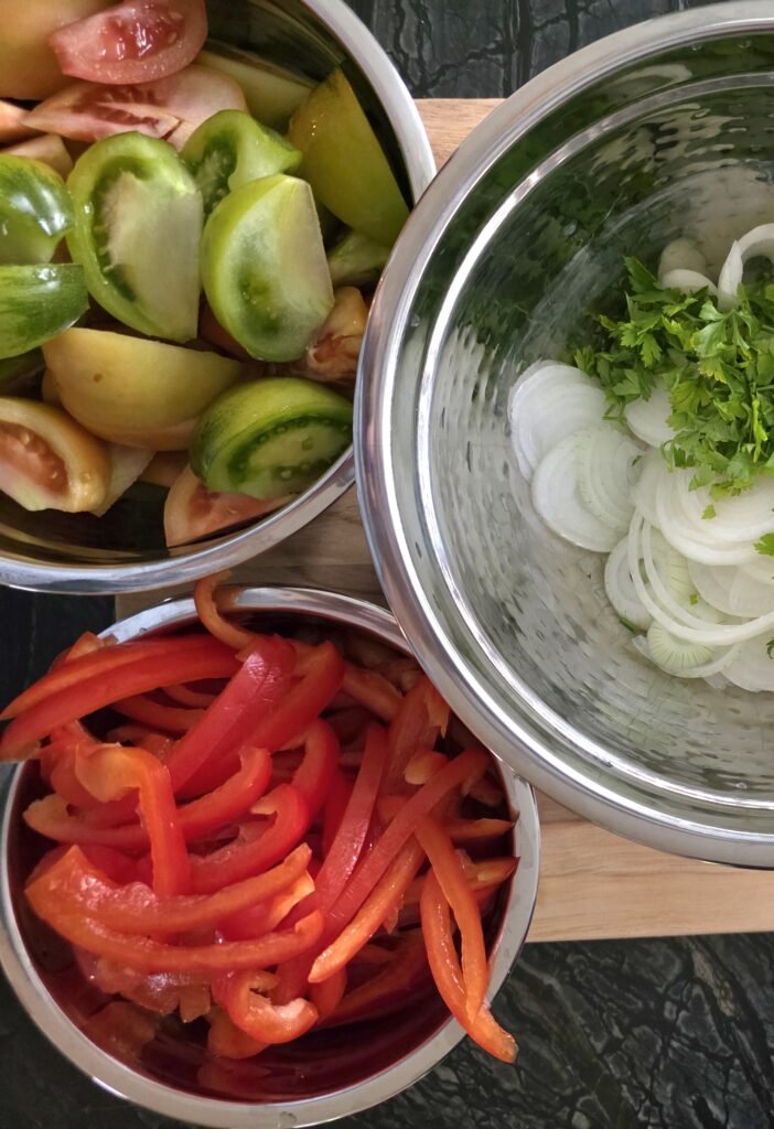 Bowls of sliced tomatoes, red pepper strips, onion rings, and chopped parsley.